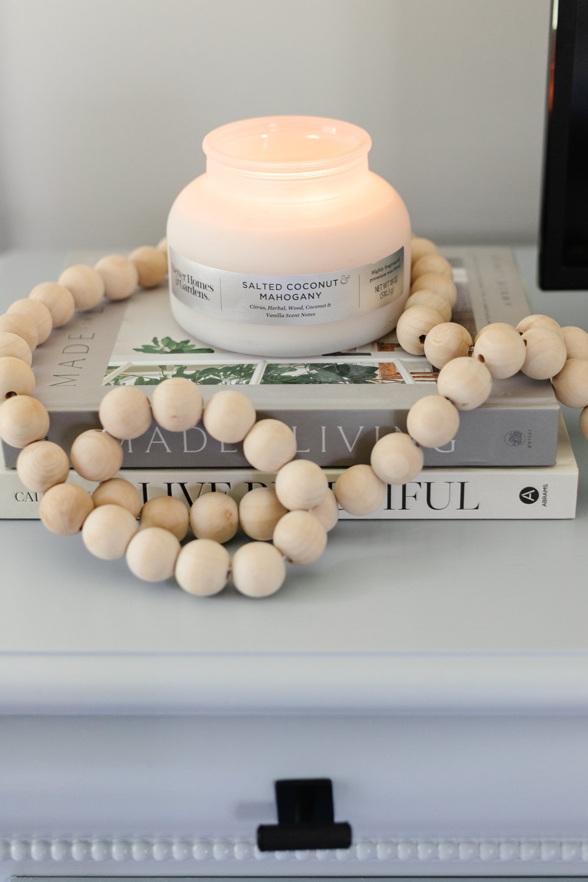 candle with wooden beads and book stack on dresser