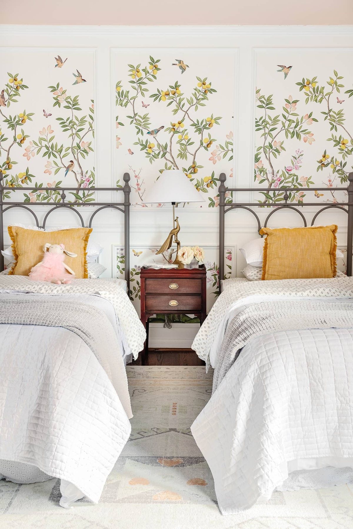 cottagecore girl's bedroom with blush pink ceiling, chinoiserie wallpaper, vintage twin beds, wood furniture, and picture frame molding