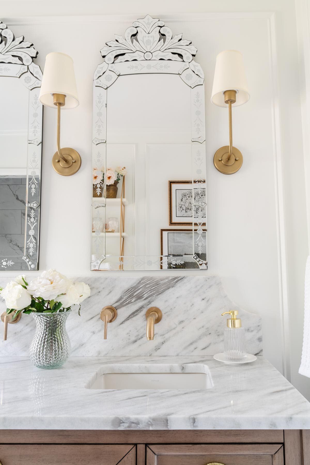 shaded vintage wall sconces on either side of a Venetian mirror in a bathroom with marble countertop