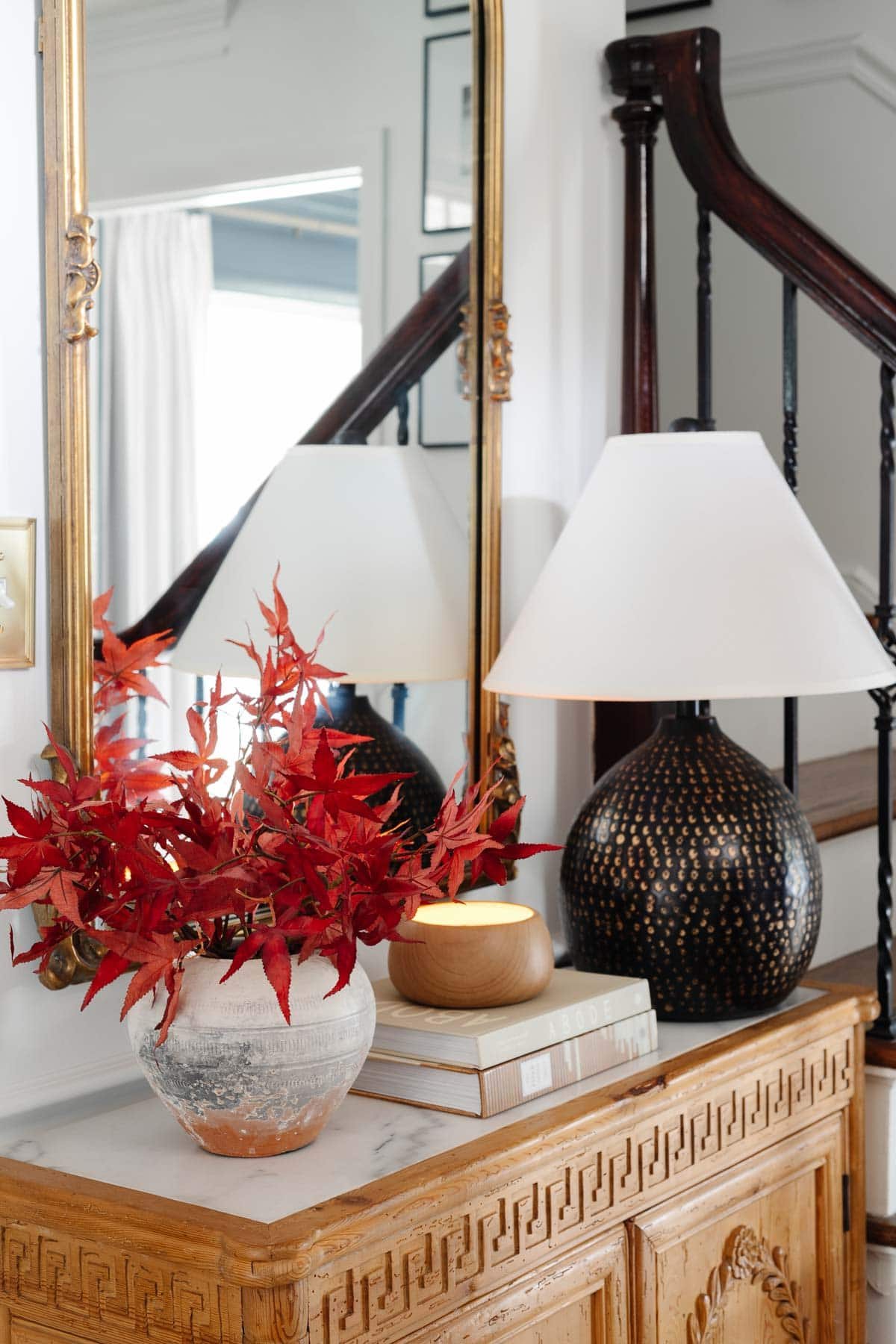 marble top entryway table with mirror, lamp, and vase of fall leaves