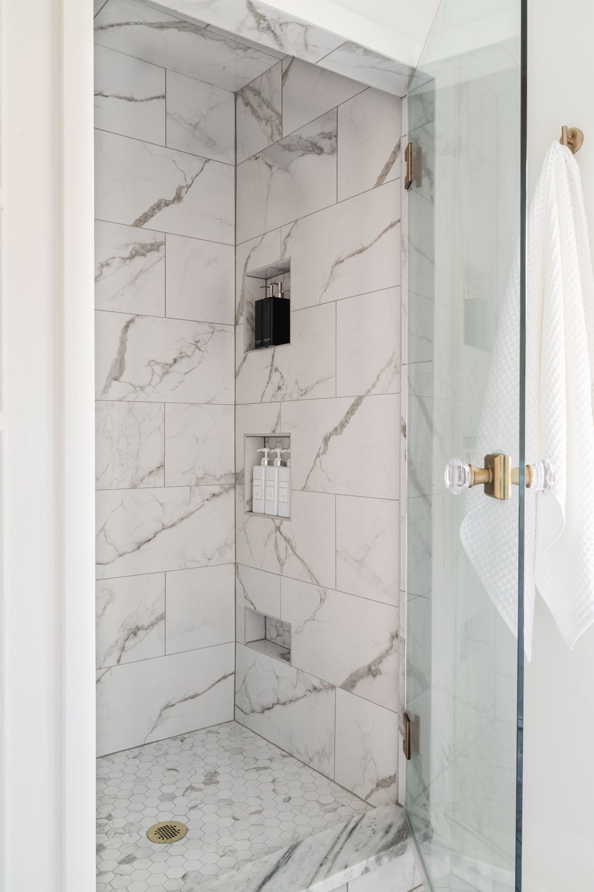 small shower with white marble effect tile and shower niches and glass door with knob