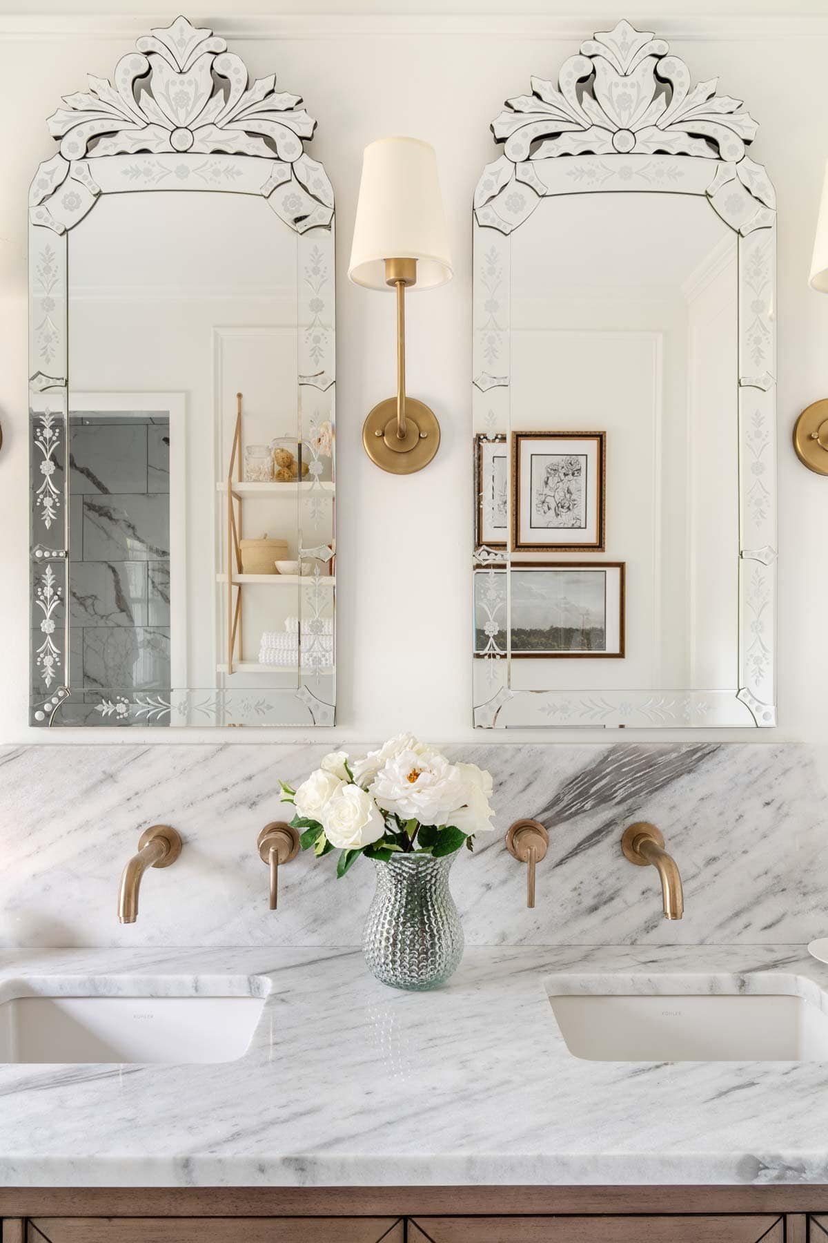 Venetian style vintage mirrors in a bathroom with gold sconces and marble backsplash