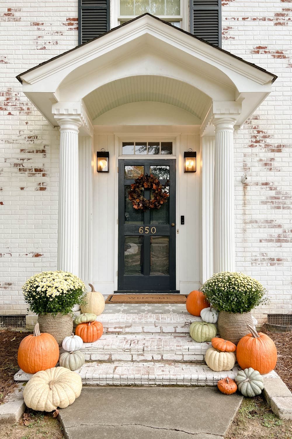 fall wreath on a front door and porch decorated with pumpkins and mums
