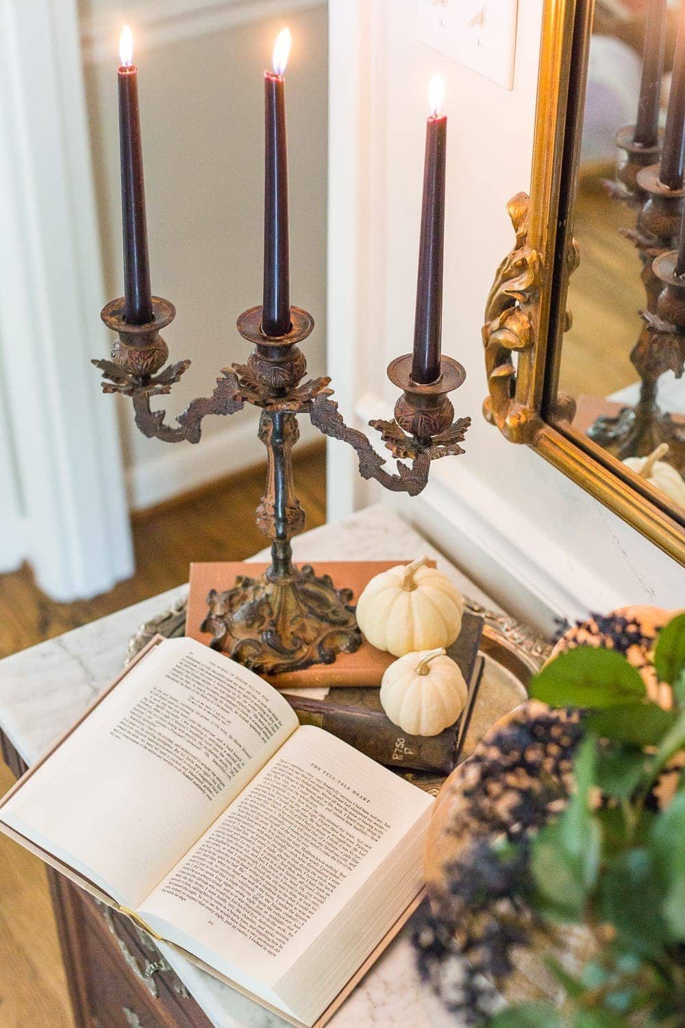 iron candelabra with black candles, silver tray, mini pumpkins, and old books for a vintage Halloween look