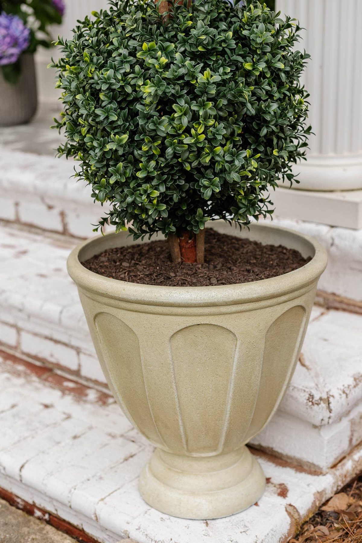resin urn planter on a front porch with faux topiary