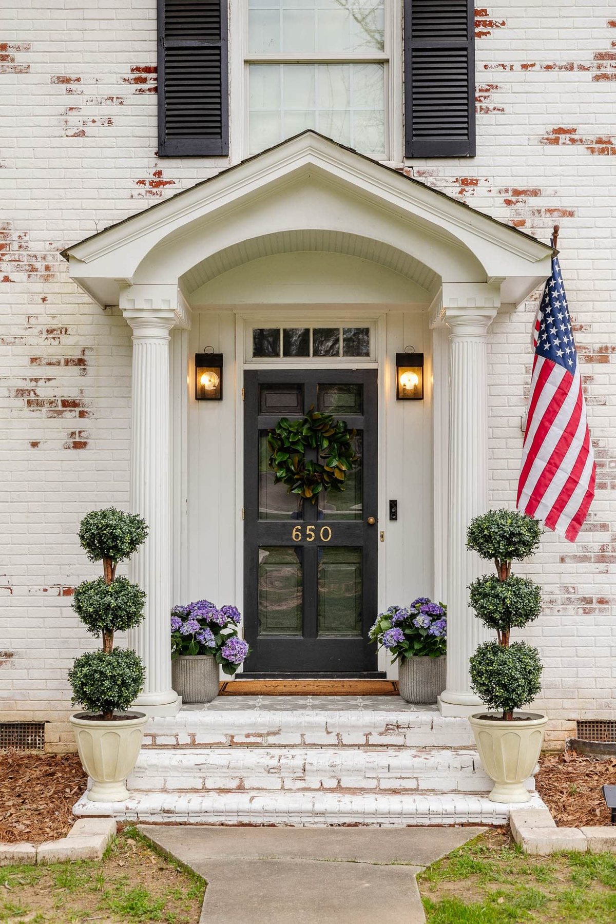 colonial small front porch on a limewashed brick house with boxwood topiaries and hydrangeas in planters