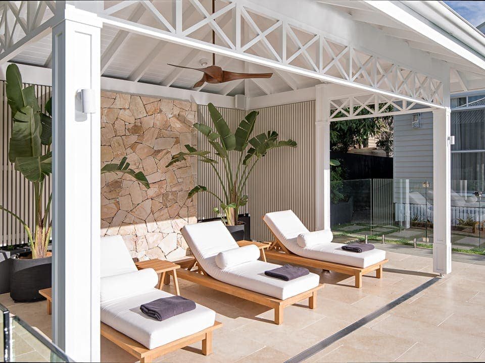 white cabana with outdoor lounge chairs and stone wall