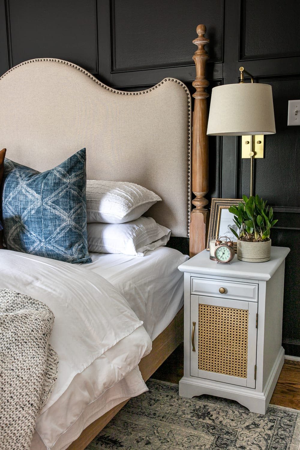 stacked pillow and throw pillows on a bed with a white cane nightstand