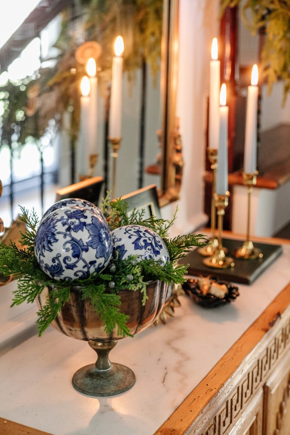 porcelain orbs in a footed bowl with greenery on an entryway table for blue and white Christmas decor