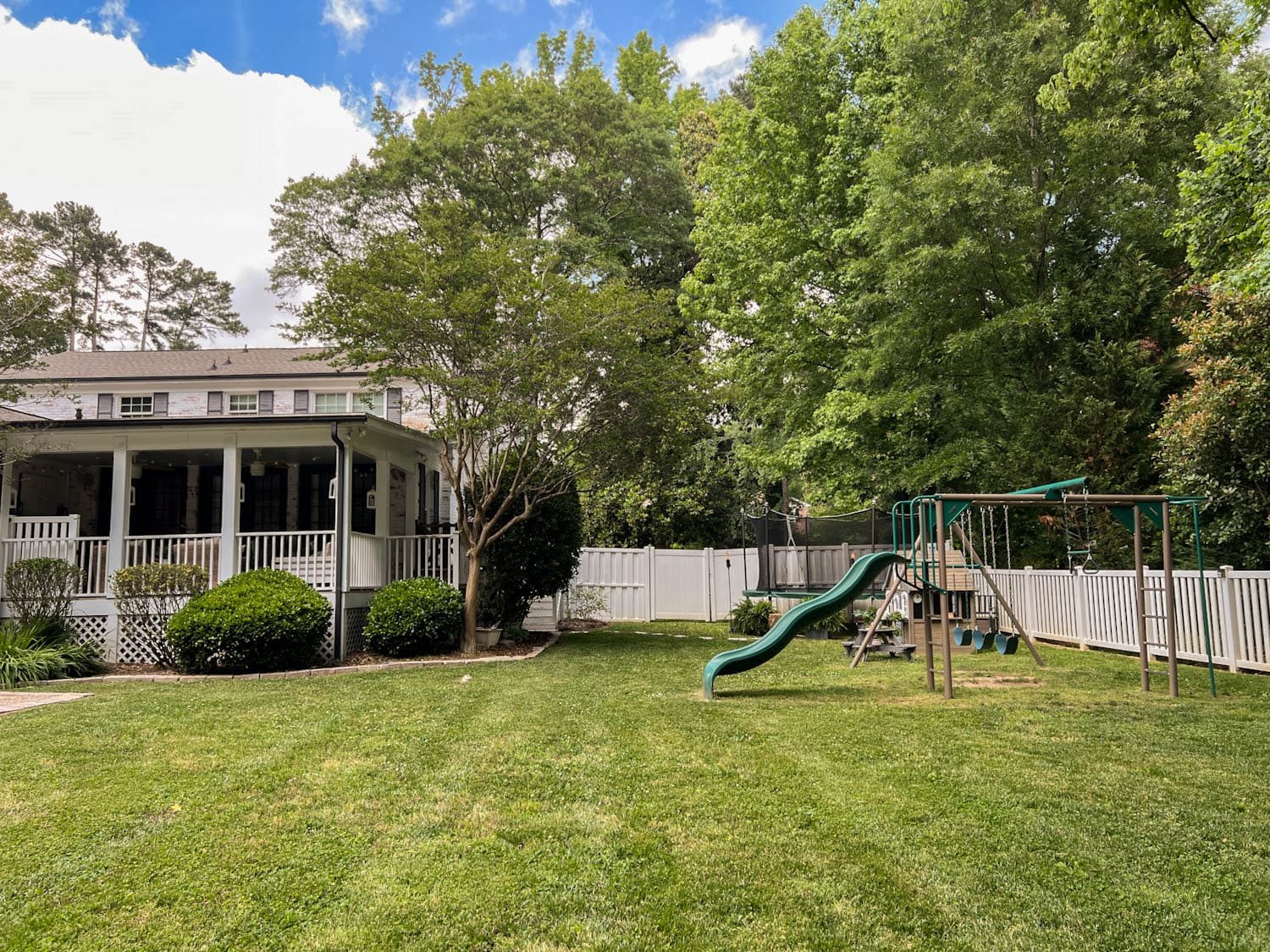 stepping stones leading to outdoor trampoline with tree stump trampoline ladder, ferns, tiki torches, playhouse, picnic table, and swing set