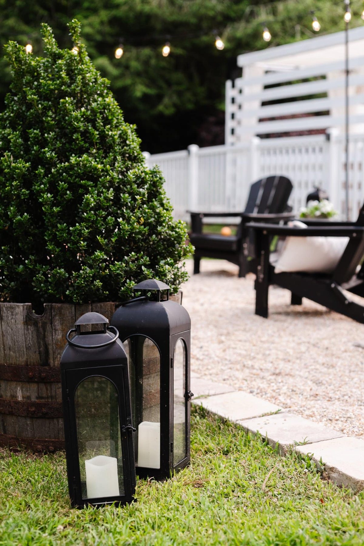 black lanterns beside a pea gravel backyard fire pit and boxwood tree