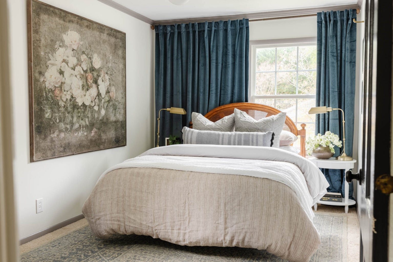 guest bedroom with blue curtains, bed in front of off center window, and oversized floral art painting
