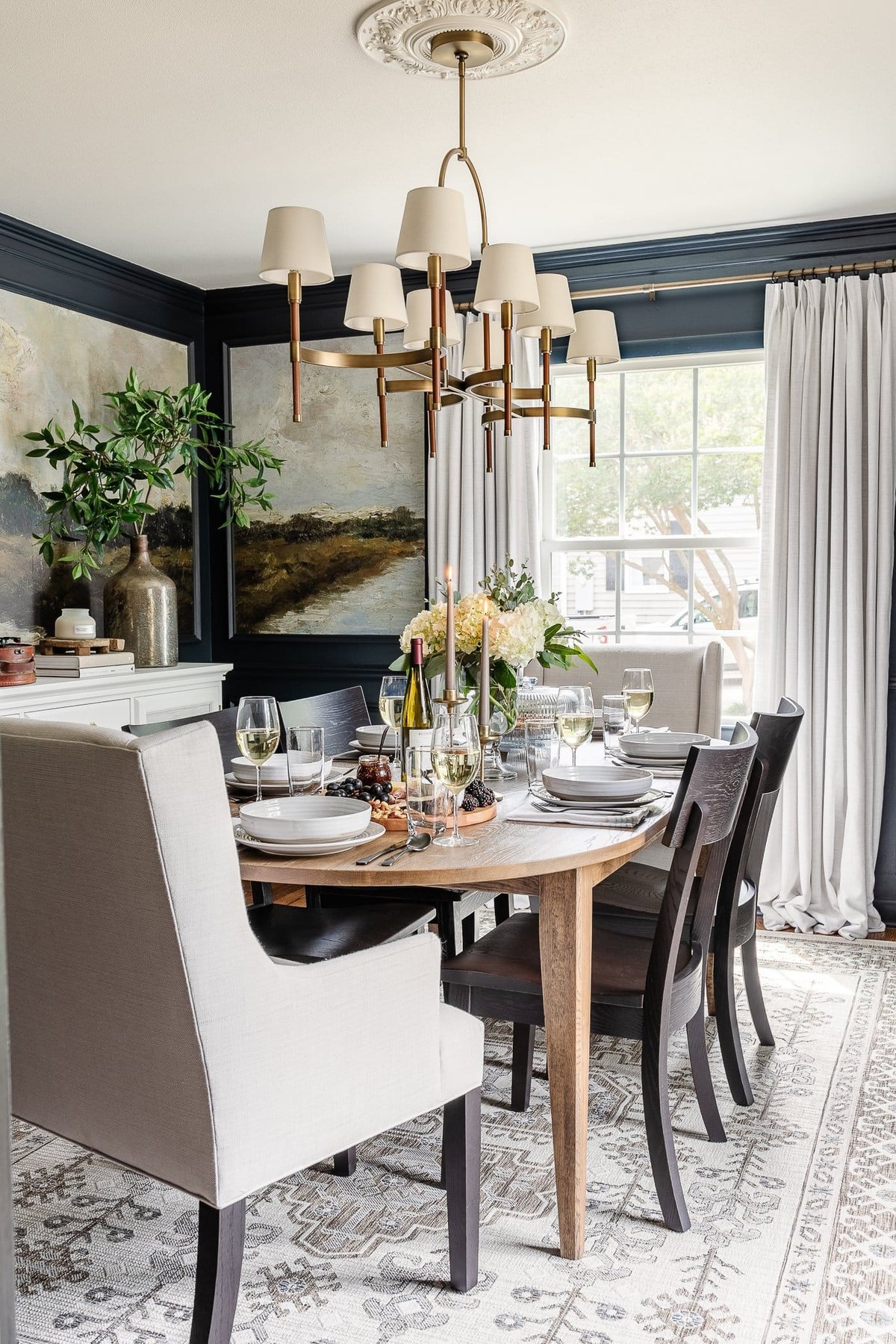 dining room with mural wallpaper, shaded chandelier, linen chairs, black chairs, oval dining table, and simple dinner table decor