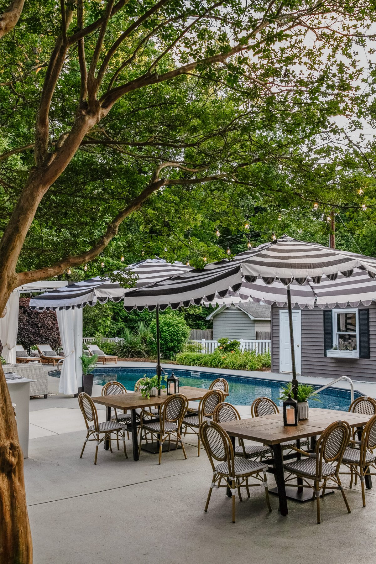 backyard swimming pool with outdoor dining sets, striped umbrella, painted vinyl siding on shed, painted concrete deck, poolside patio furniture and cabana