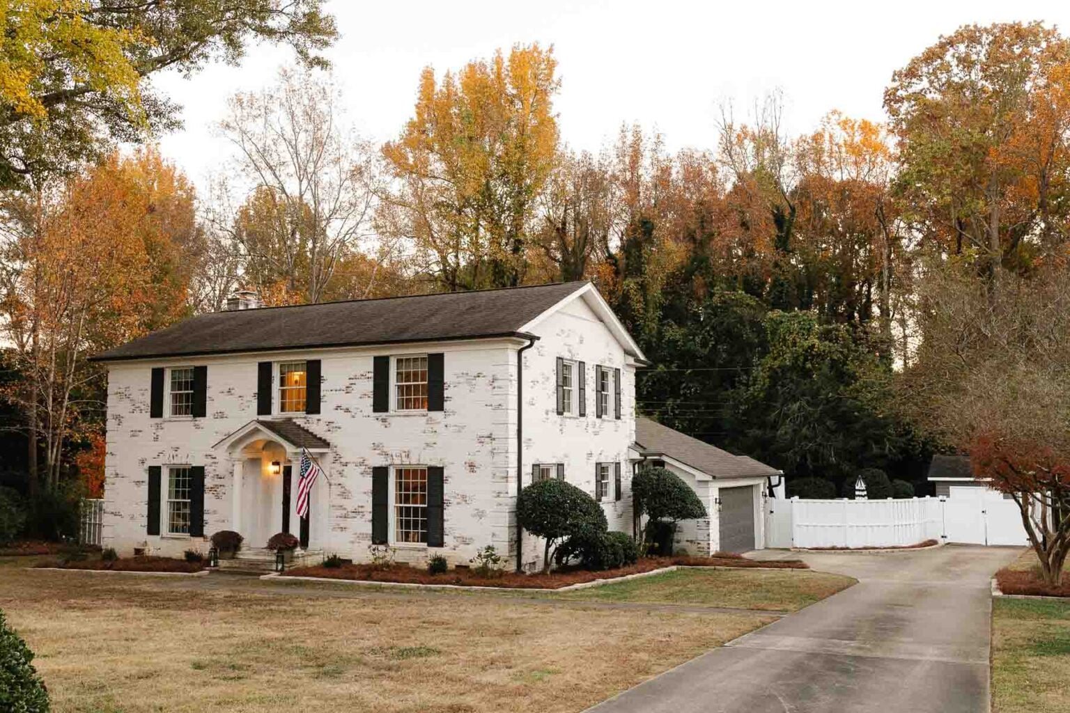 white limewashed brick colonial house with black shutters and black doors and white vinyl fence