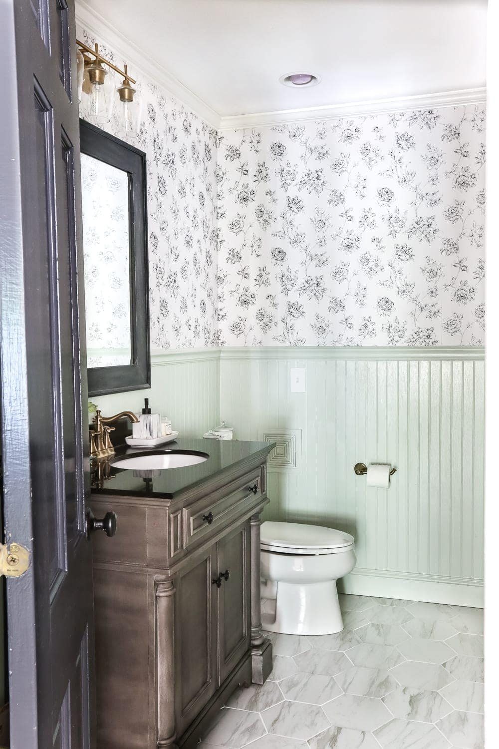mint green beadboard in a half bath with black and white floral wallpaper, faux marble hexagon tile floor, and wood vanity