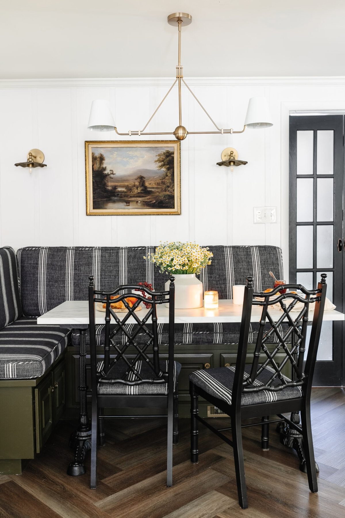 cottagecore breakfast nook with banquette, shaded chandelier, bifold French door, herringbone floor, and marble bistro table
