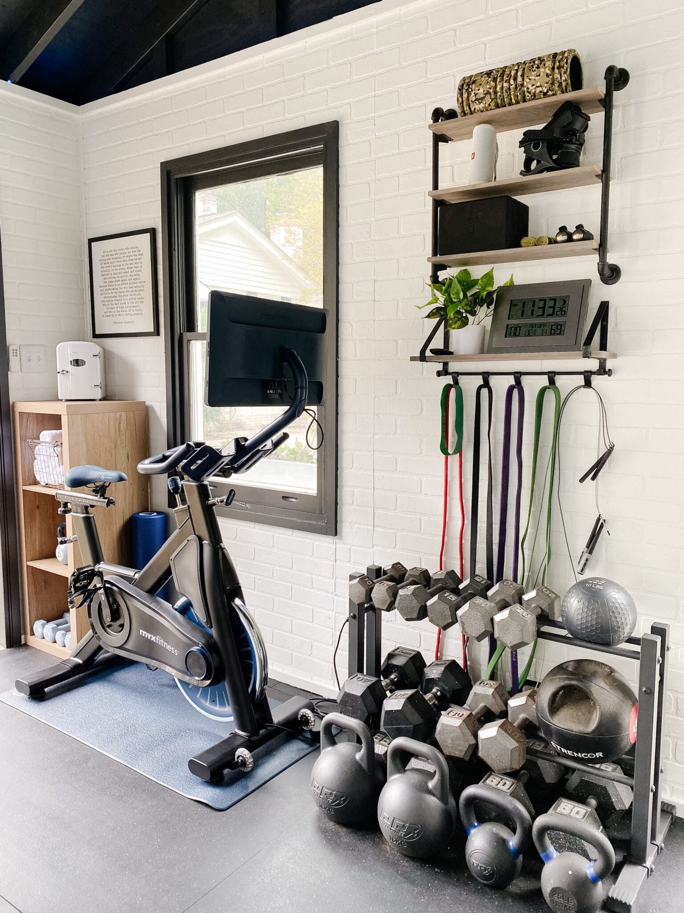 home gym made from a backyard shed with faux brick walls, black vaulted ceiling, and black rubber floors