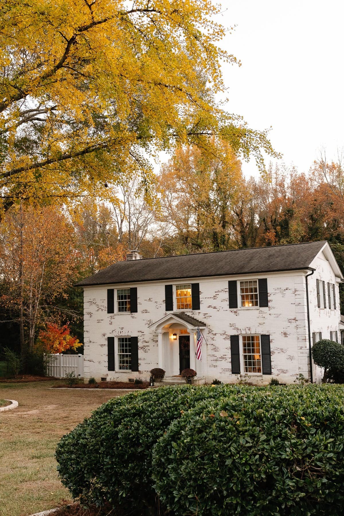 white limewashed brick colonial house with black shutters and black doors and white vinyl fence