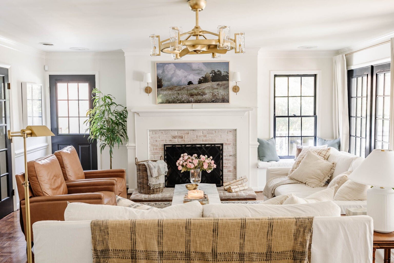 white living room with limewashed brick fireplace, gold fandelier, white Pottery Barn sofas, leather recliners, art TV, and black French doors