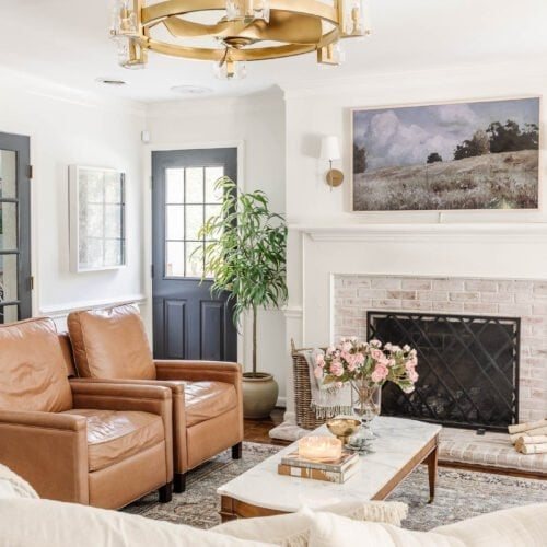 glass and gold fandelier in a living room with limewashed brick fireplace white walls and black doors