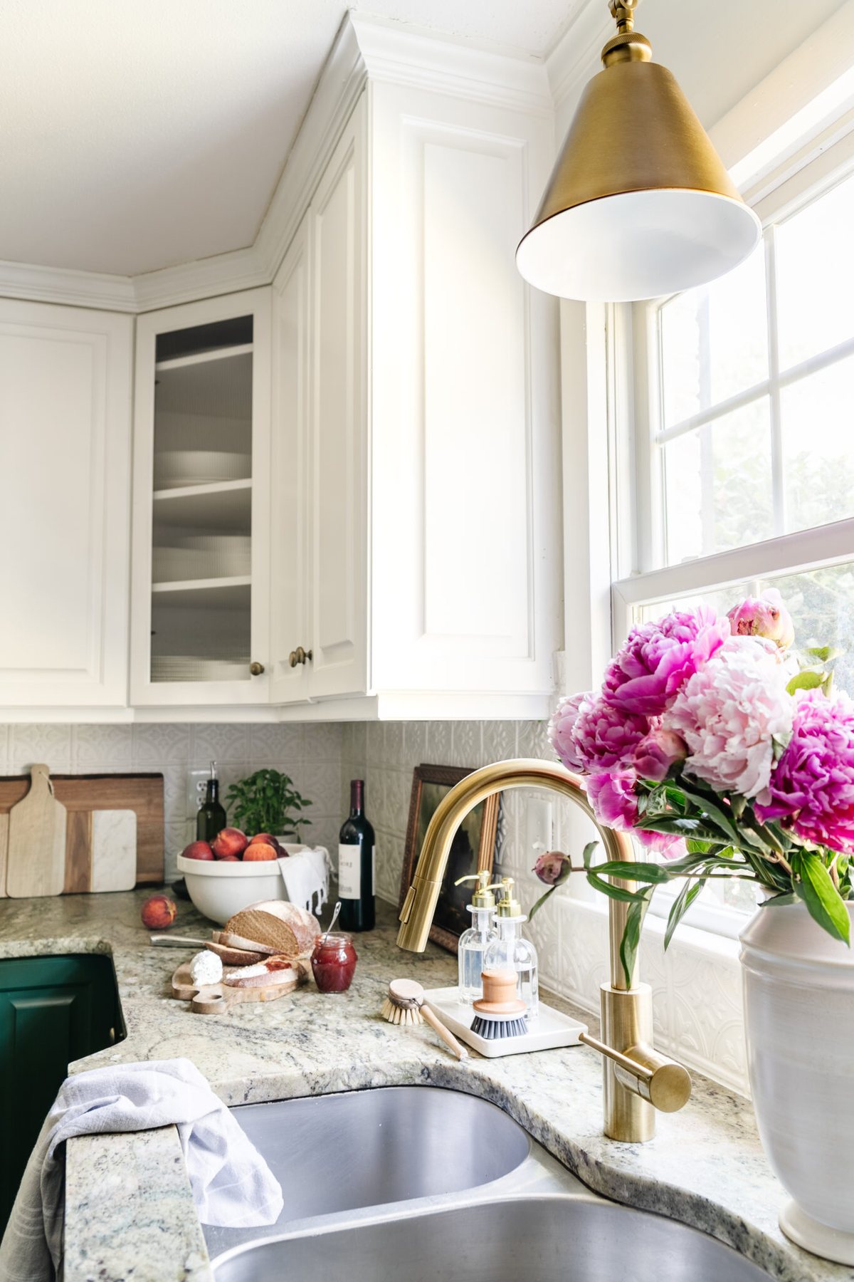kitchen sink in front of window with brass faucet and brass pendant light