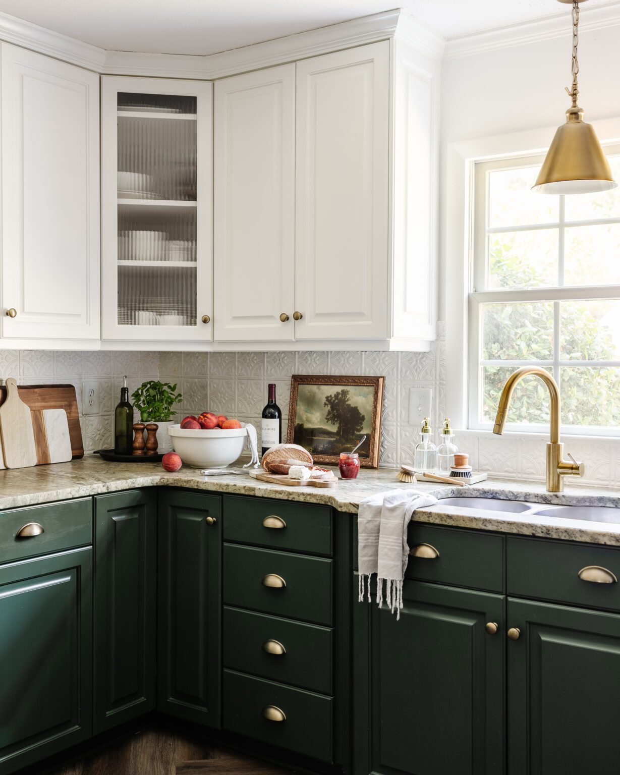 leathered granite kitchen countertop, cottagecore style countertop decor, and kitchen sink with brass faucet in front of window