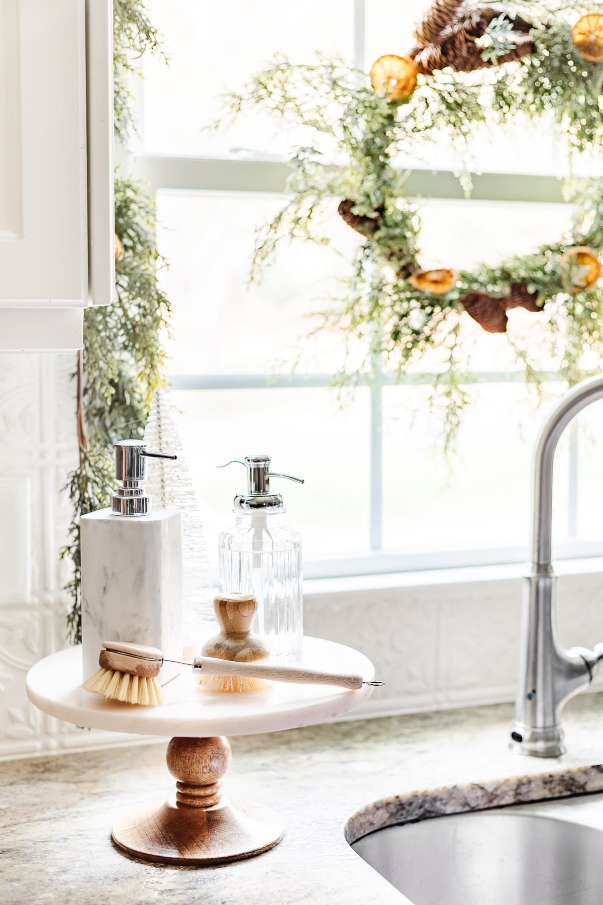 cake stand next to kitchen sink with soaps and bottle brush tree