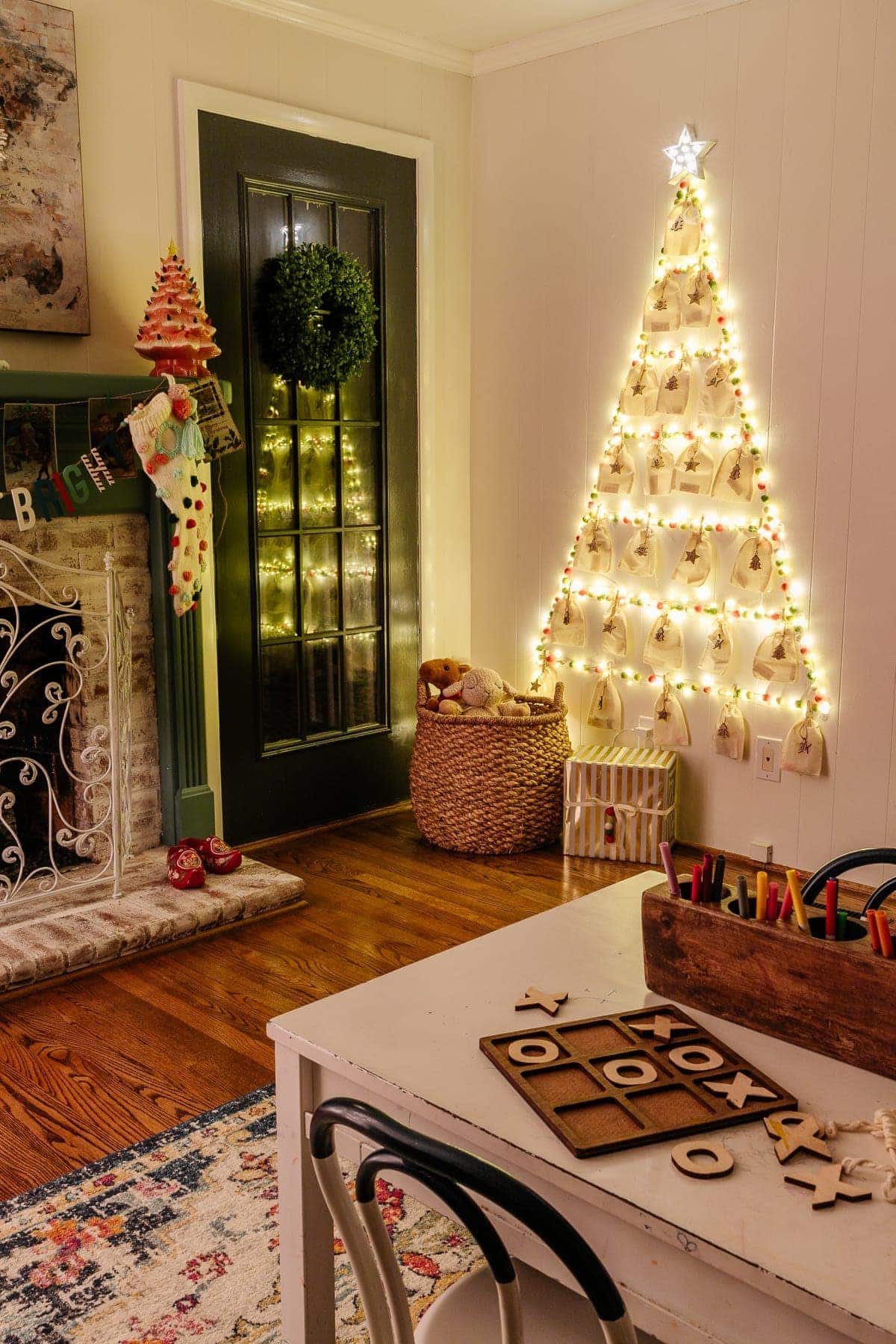 Christmas tree wall display made with fairy lights, pom pom garland, and Command hooks in a playroom