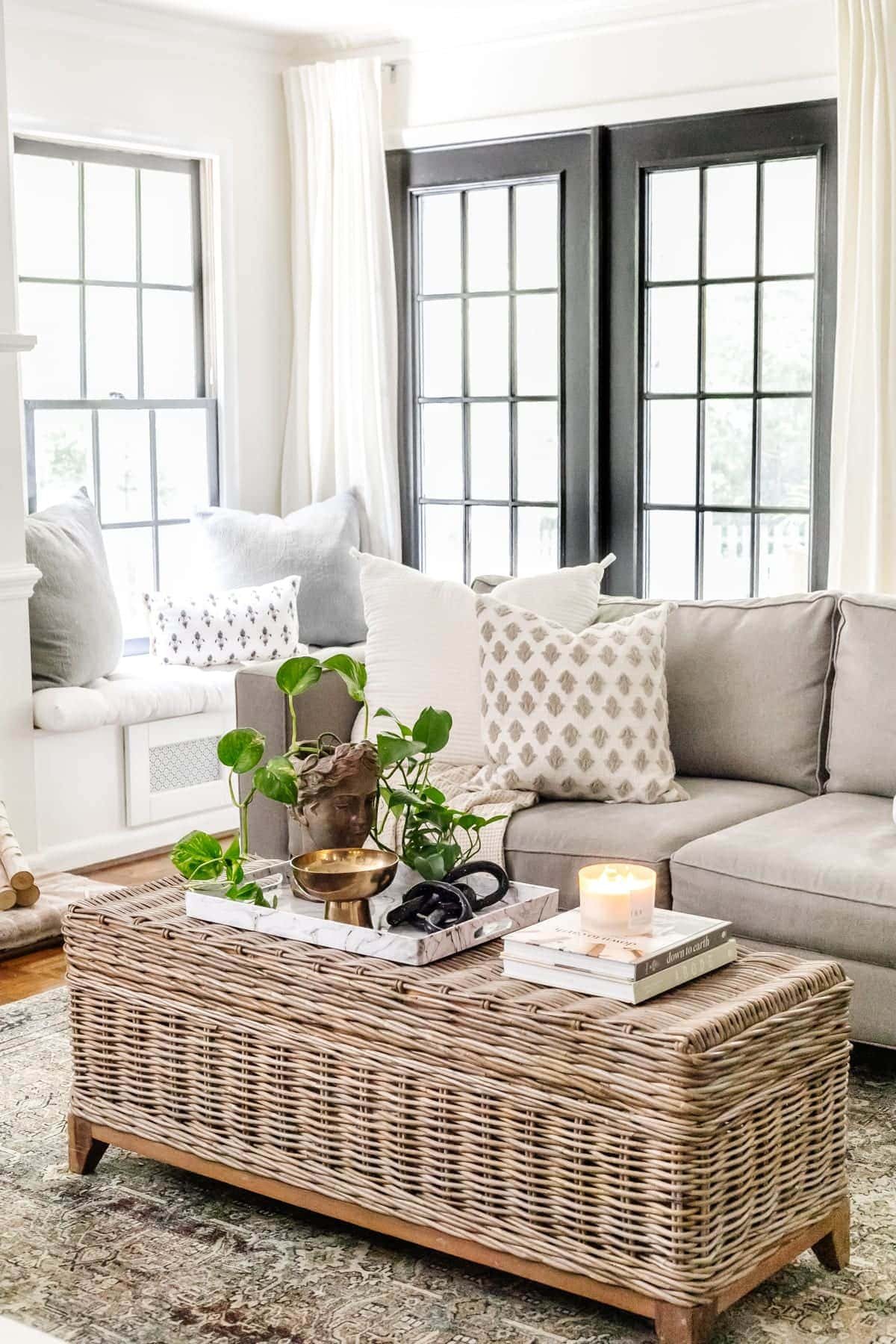 rattan coffee table in a living room with black doors, bust planter, and marble tray