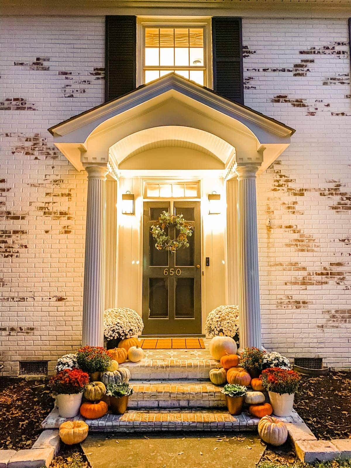 fall porch at night with pumpkins and mums and limewashed brick