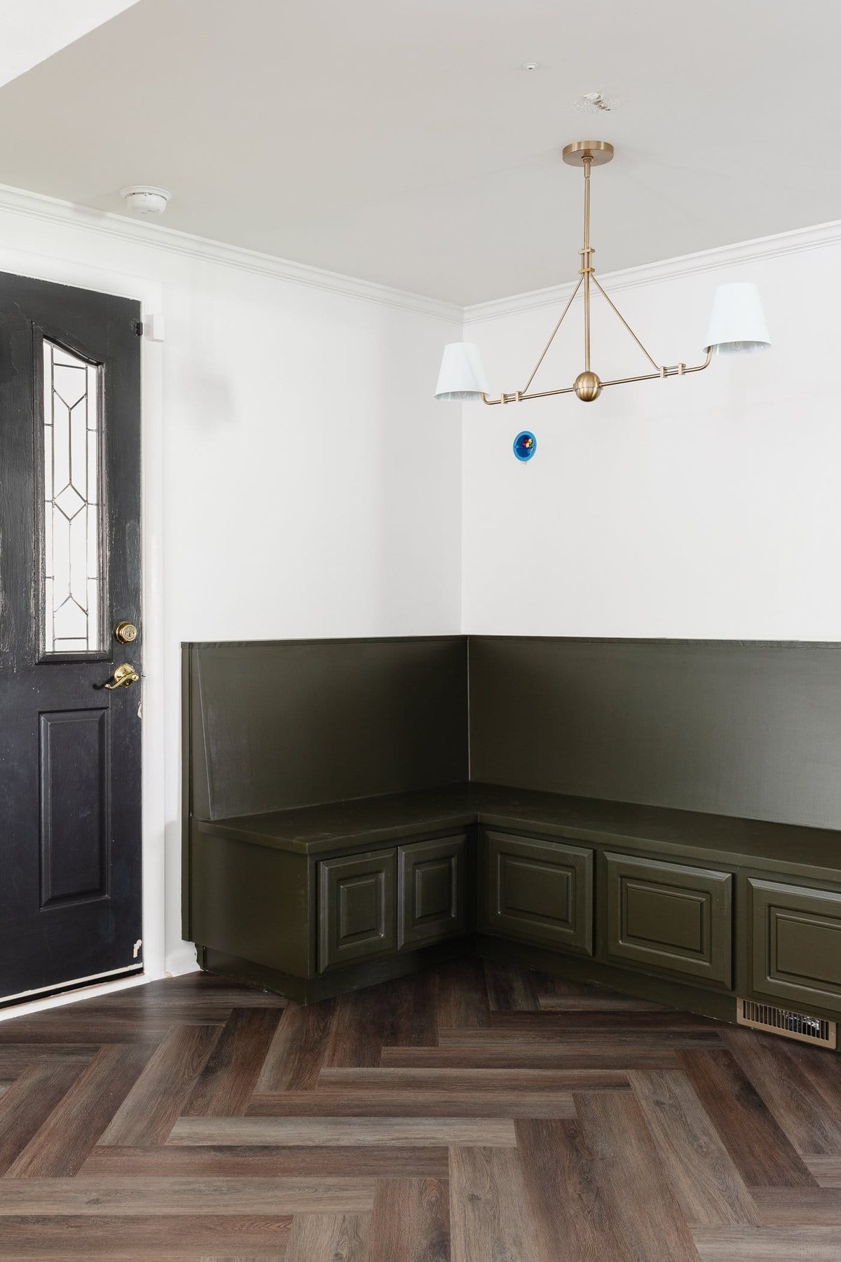 breakfast nook banquette painted olive green with shaded linear chandelier and herringbone floors