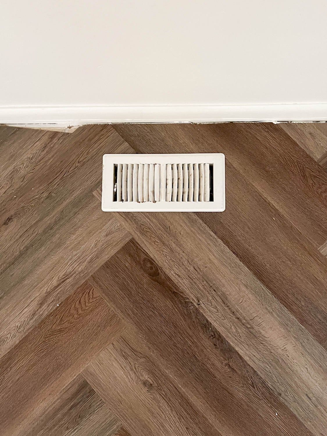 floor vent against a wall on herringbone flooring