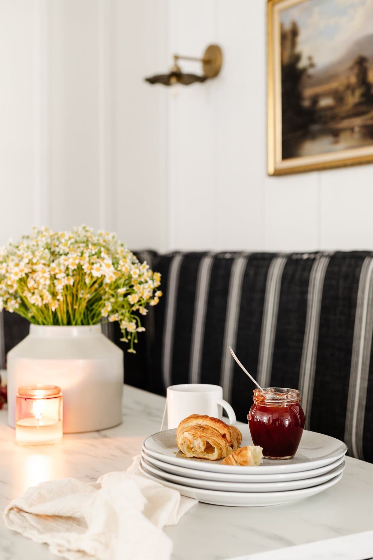 breakfast table decor - vase of daisies, wood cutting board with croissants, bowl of grapes, and candle