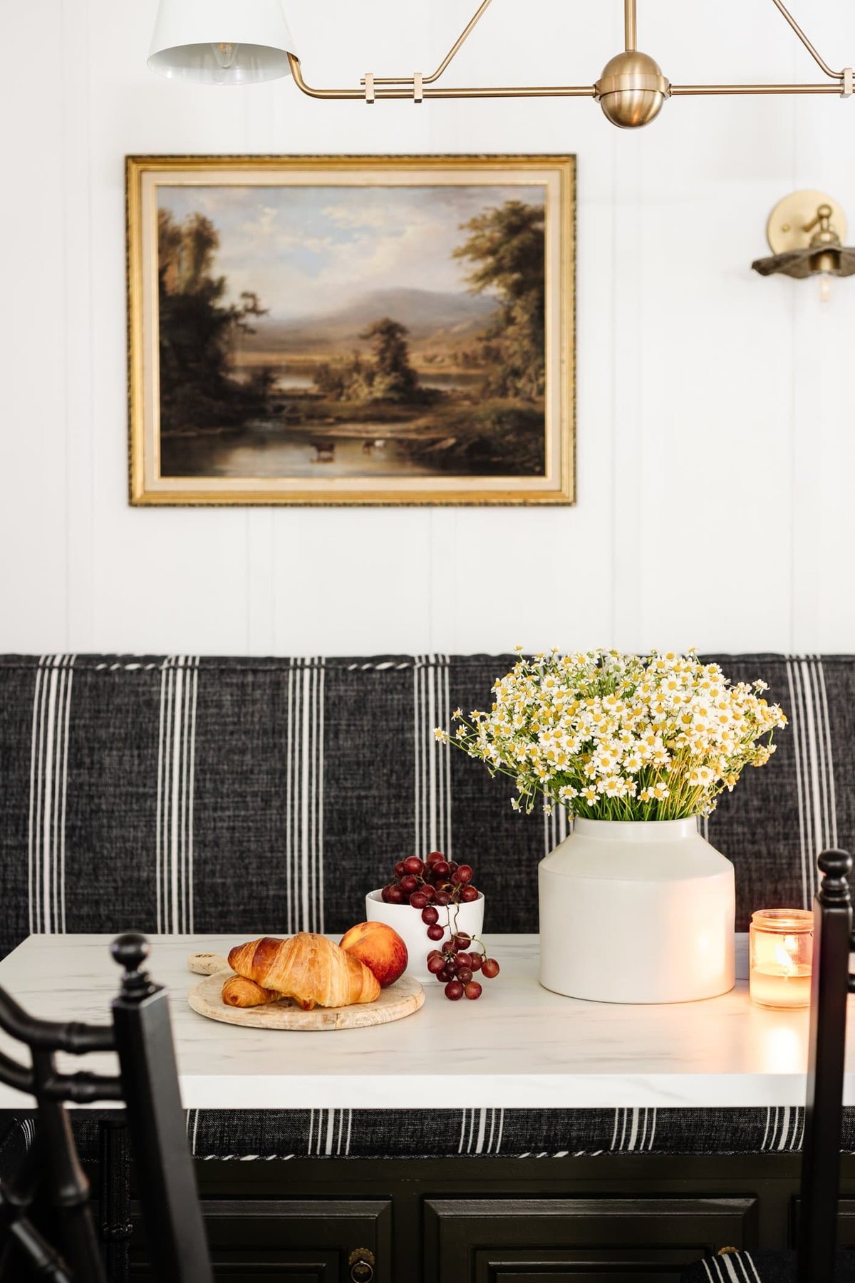breakfast table decor - vase of daisies, wood cutting board with croissants, bowl of grapes, and candle