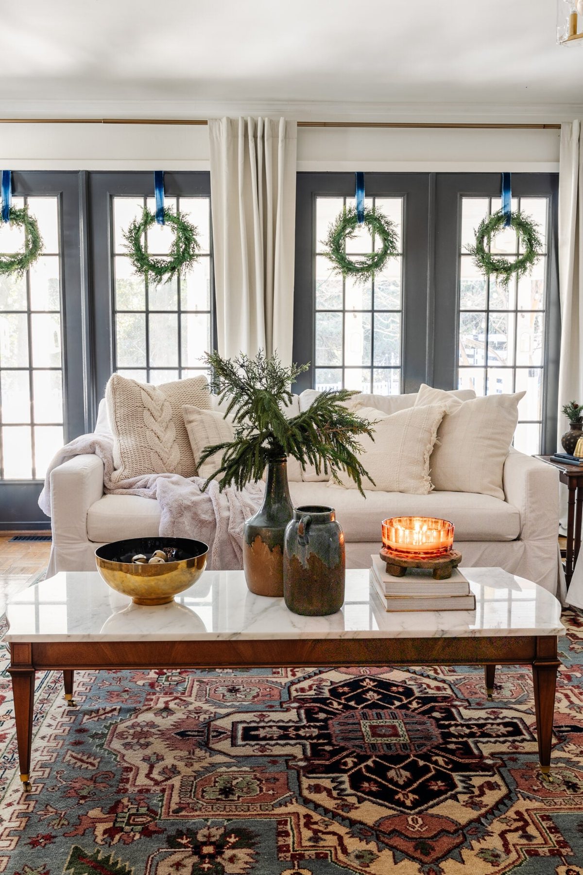 marble top coffee table with Christmas greenery in vase, bowl of jingle bells, and candle