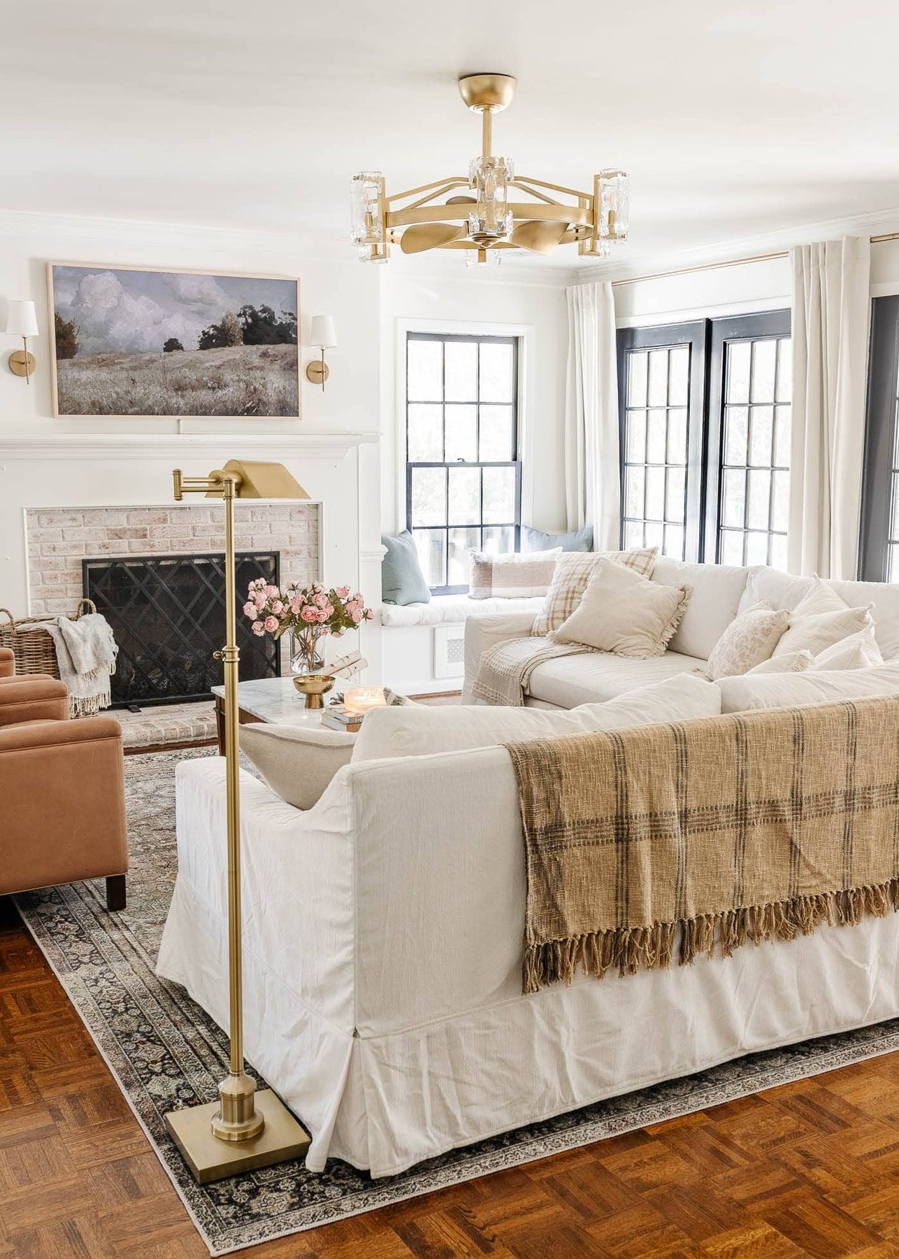 white living room with limewashed brick fireplace, gold fandelier, white Pottery Barn sofas, leather recliners, art TV, and black French doors
