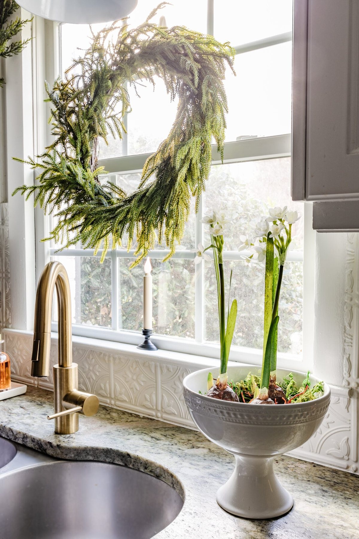 pedestal bowl of paperwhite flowers beside a kitchen sink
