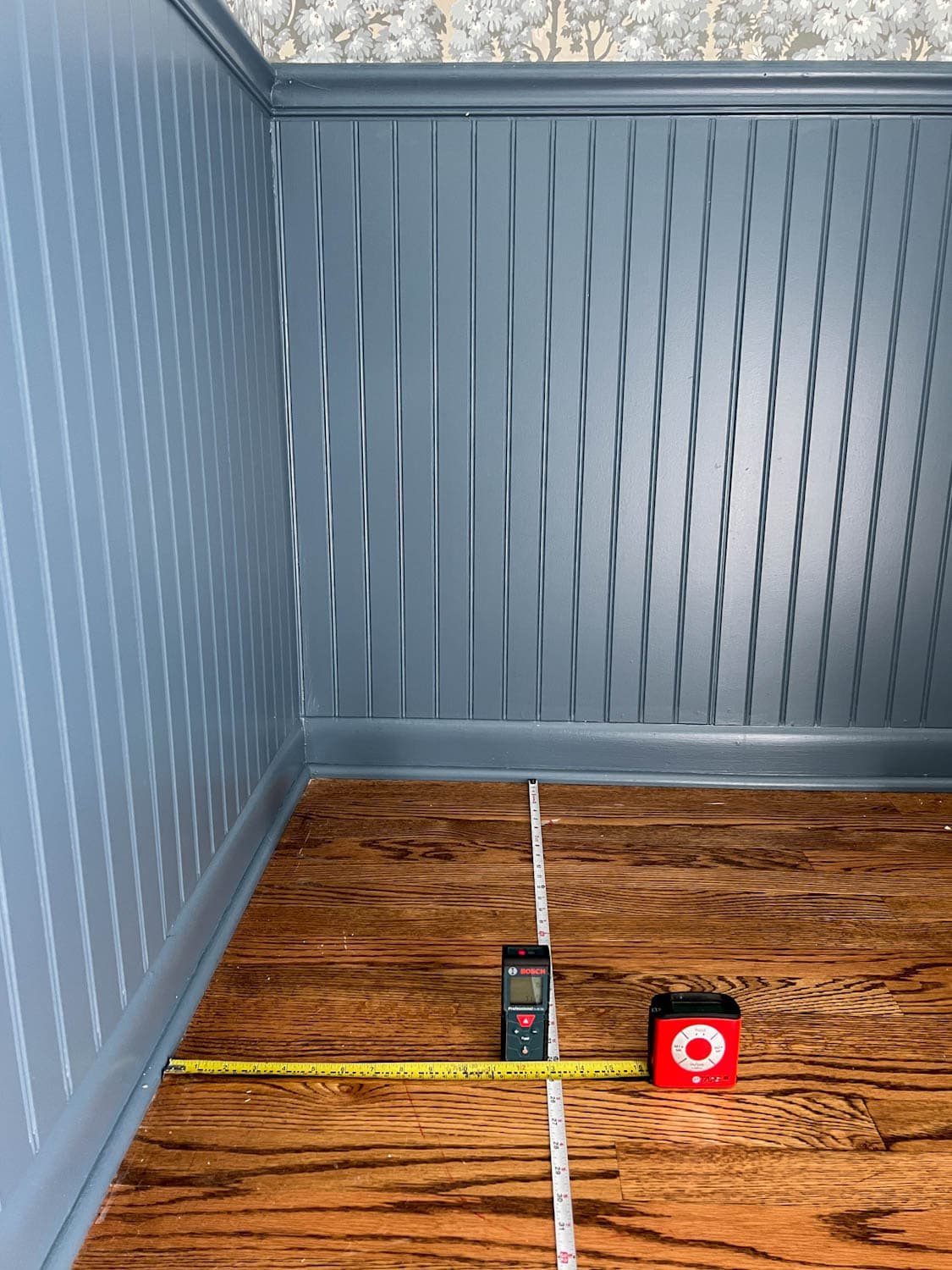 measuring and marking a block print pattern wallpaper on a ceiling using two tape measures and a laser