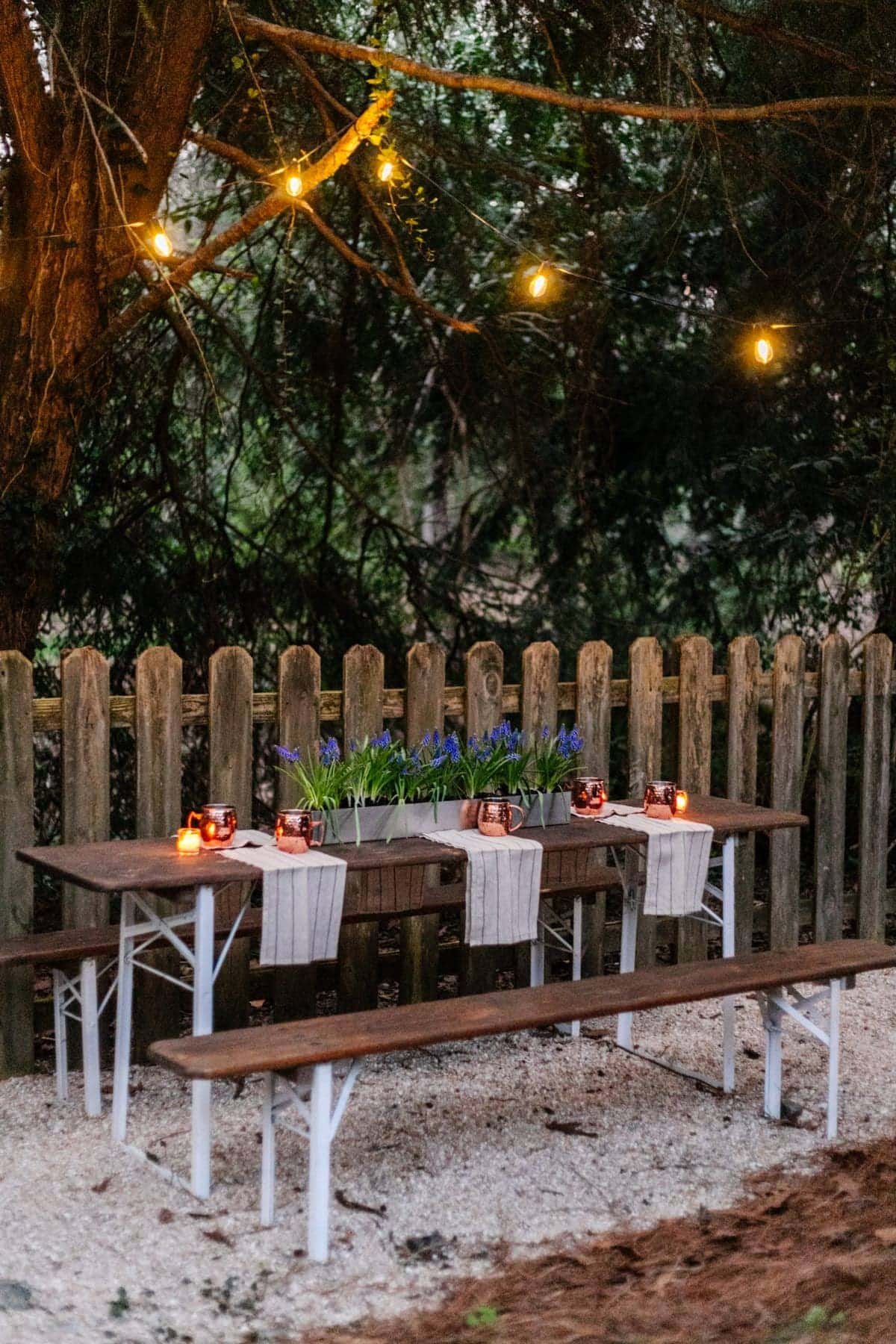 hanging solar string lights in trees above a folding table to make a backyard beer garden dining area
