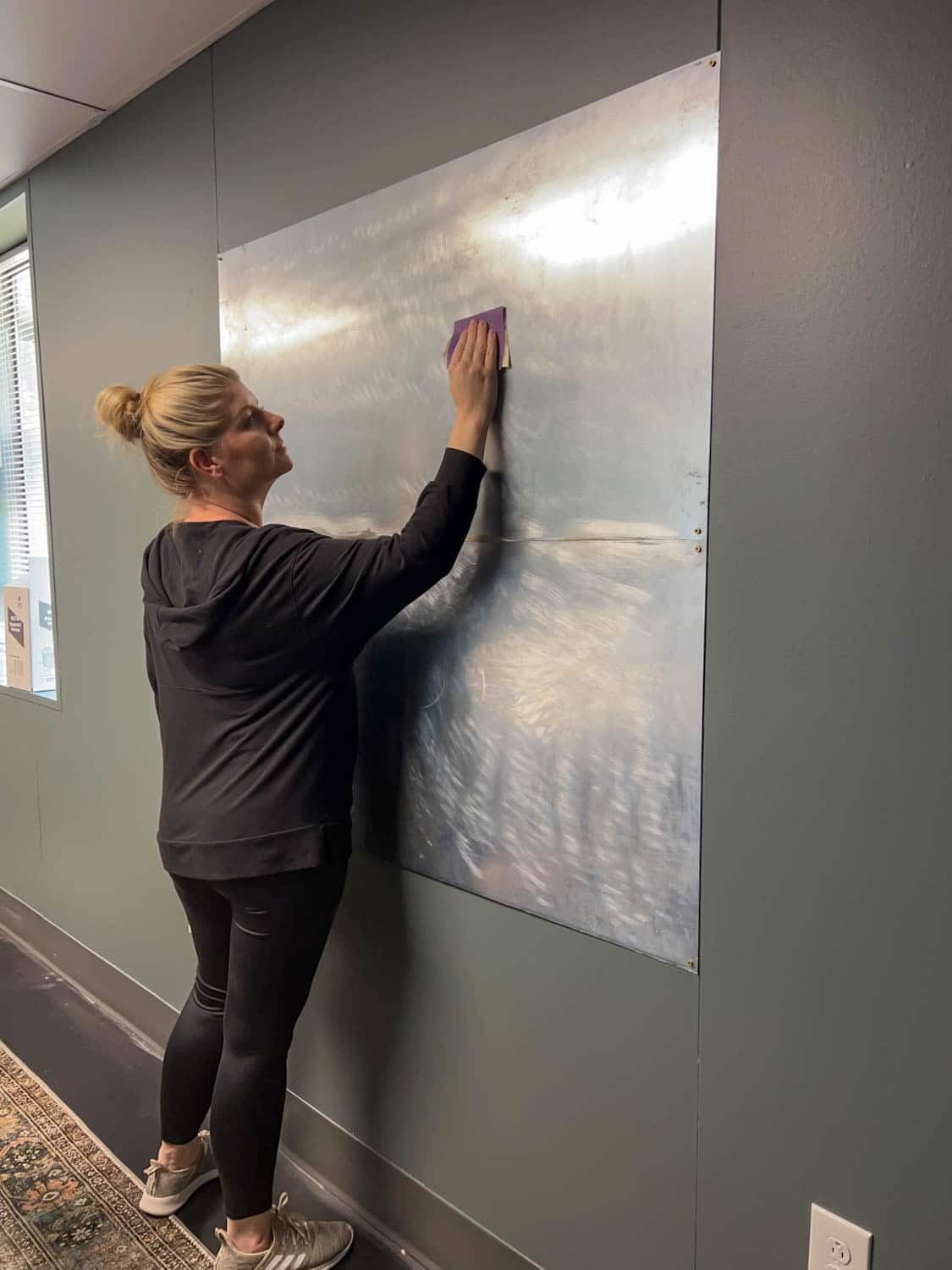 sanding metal sheets on a wall to apply a mural as DIY art