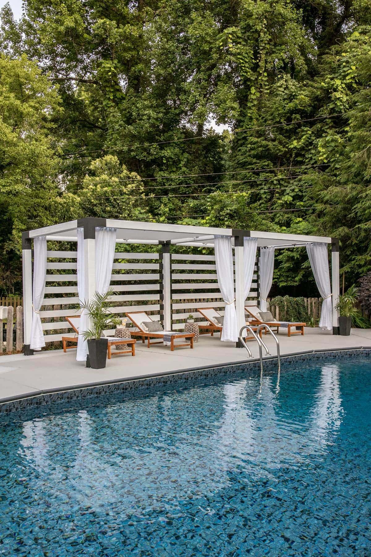 white DIY pergola cabana with outdoor curtains and lounge chairs