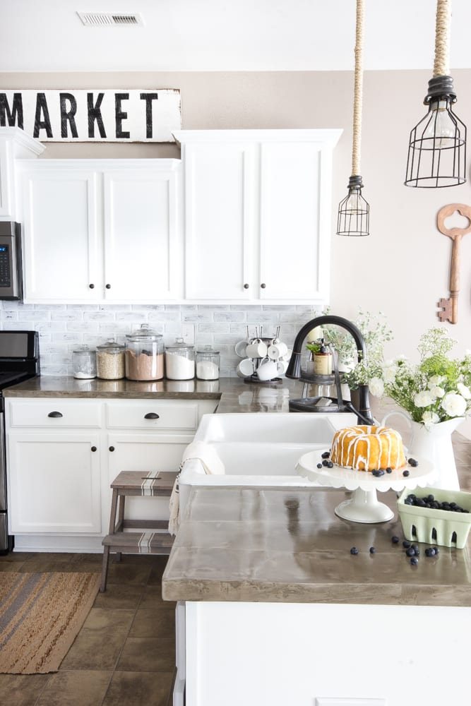 modern farmhouse kitchen with faux brick backsplash, concrete countertops, and white cabinets