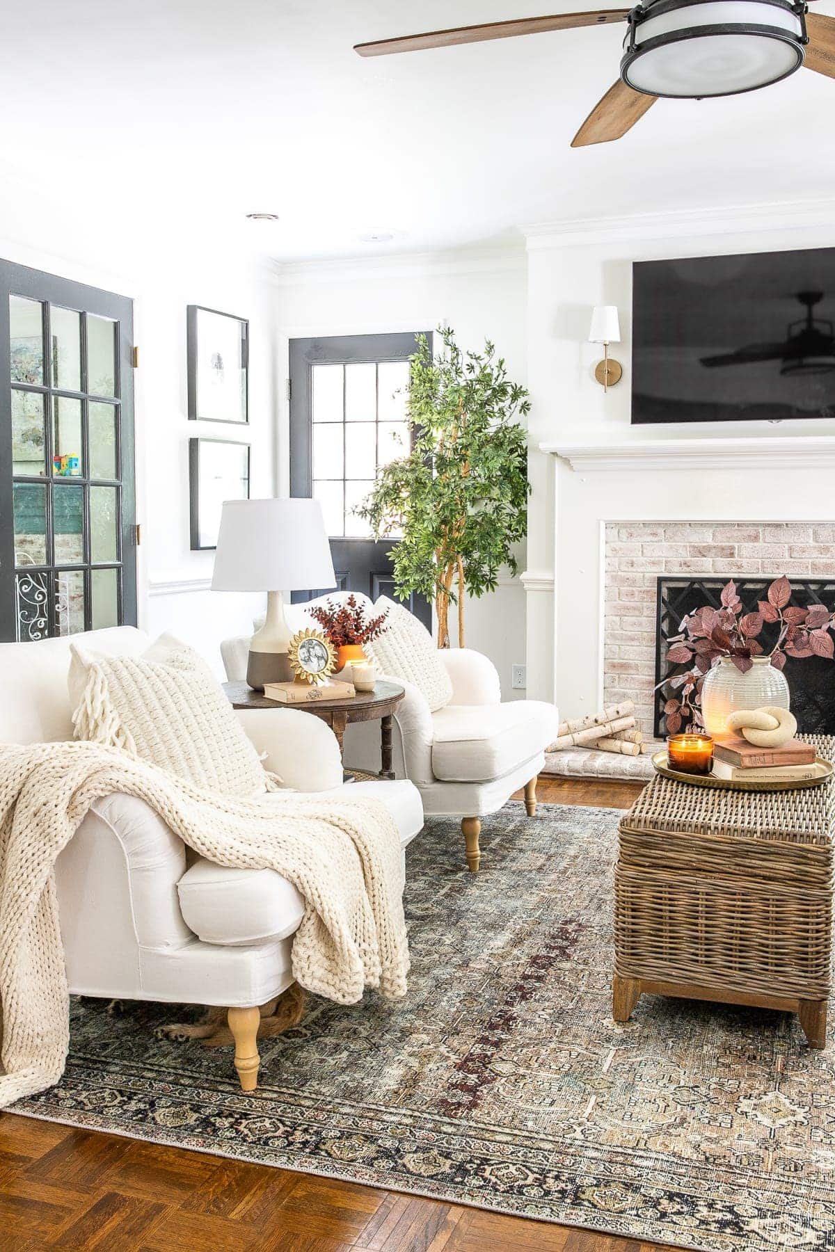 living room decorated for fall with rust and olive vintage style rug ceiling fan and TV above fireplace