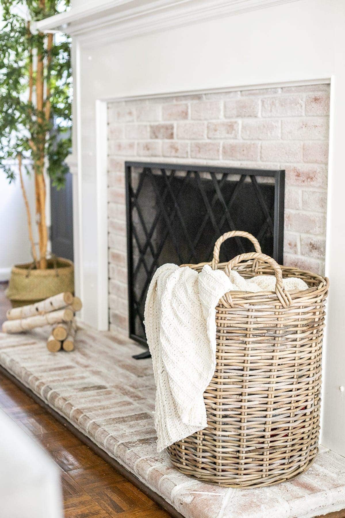 woven basket with cable knit throw blanket on limewashed brick fireplace