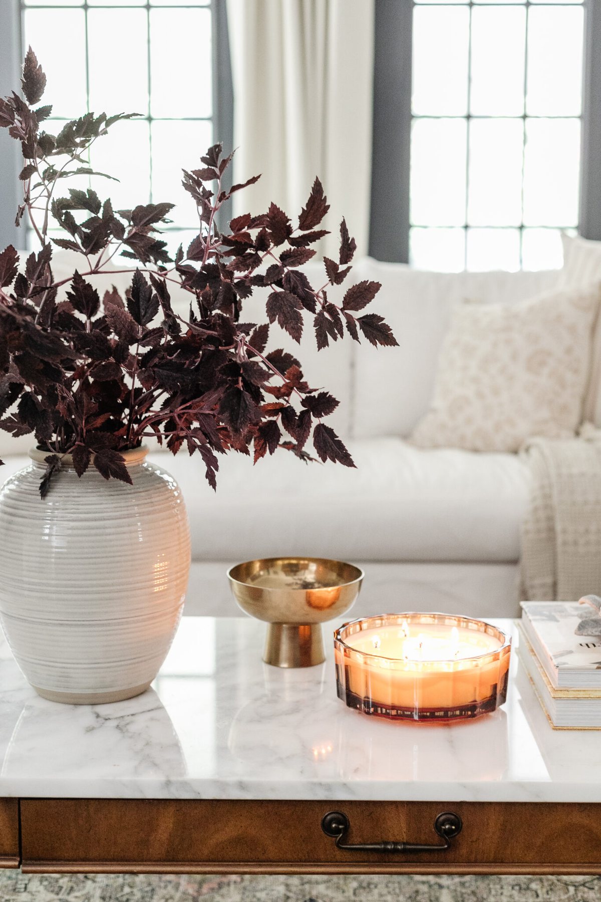fall decor on a coffee table with vase of fall branches, candle, brass bowl, and books