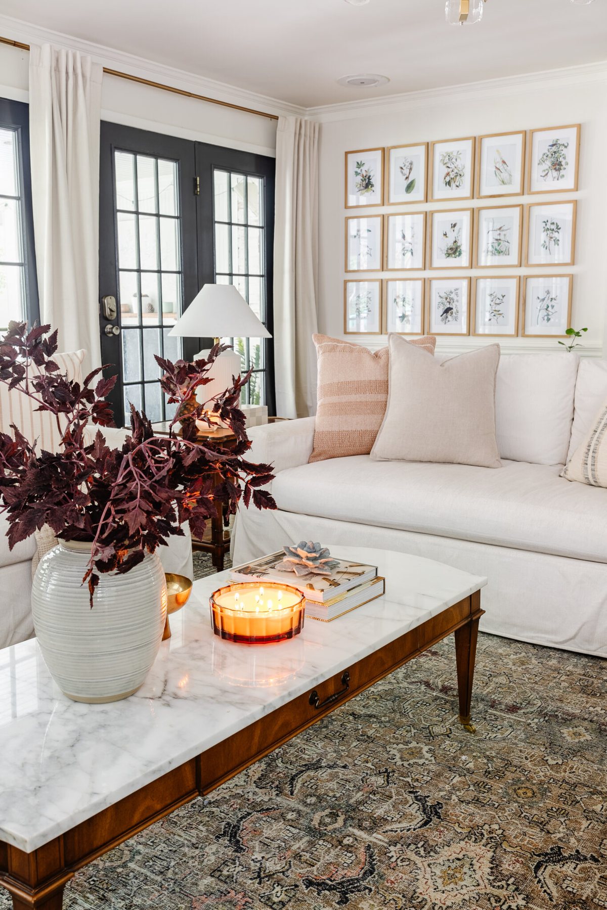 coffee table fall decor with vase of fall stems, candle, bowl, and books in front of white sofa with neutral pillows