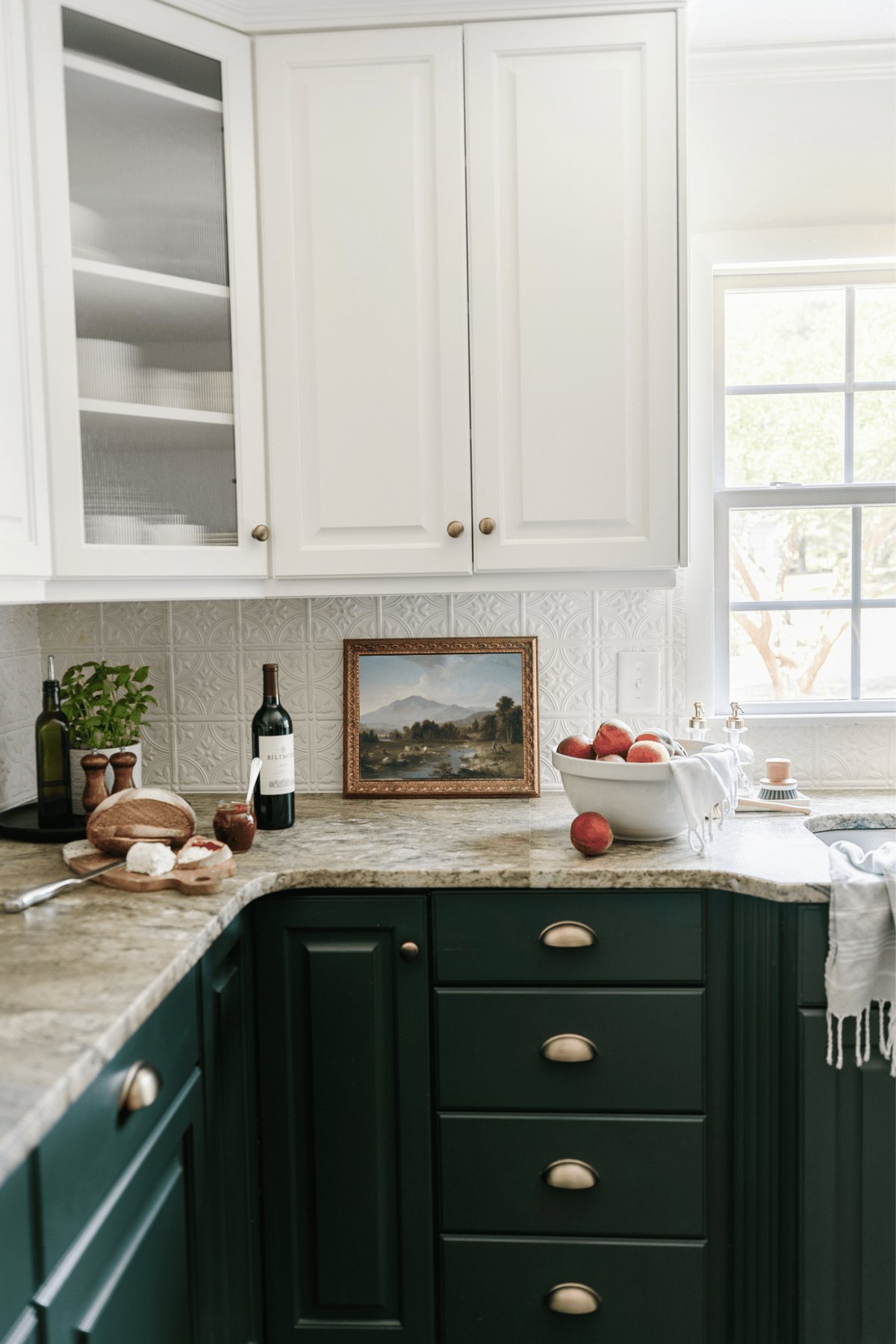 framed landscape oil painting print as kitchen art on a countertop with bowl of peaches and tray with a plant