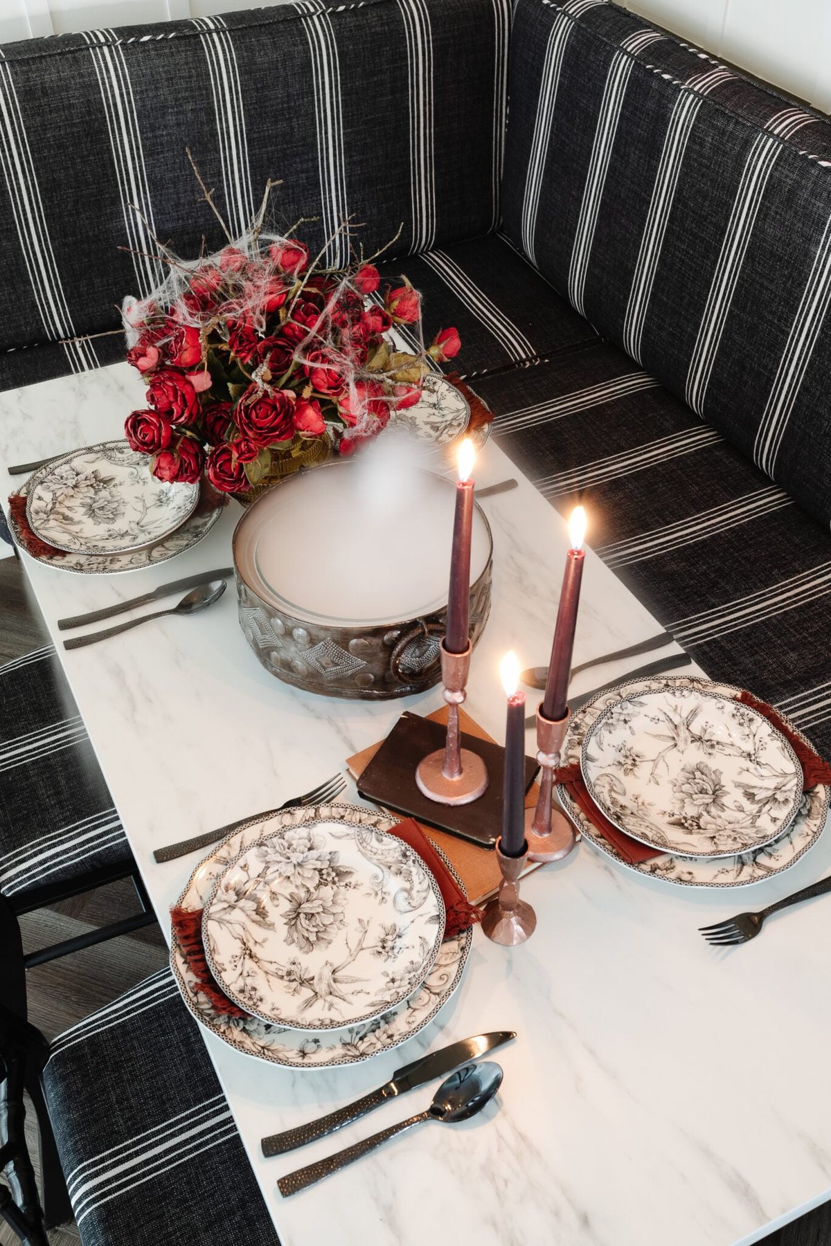 murder mystery party table decor with black toile dinnerware, cauldron of dry ice fog, and red roses with spider webs