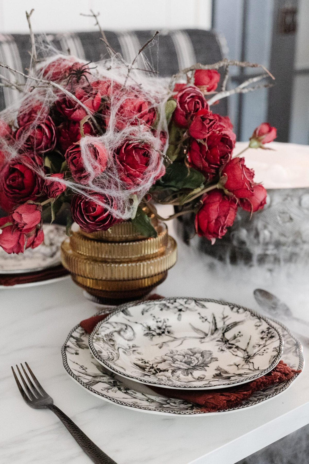 black toile dinnerware and fluted vase of red roses with spider webs